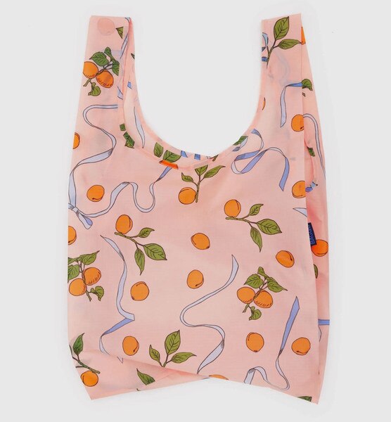 Peach-colored reusable BAGGU bag with allover orange fruit and green leaf print, accented with blue ribbon graphics,